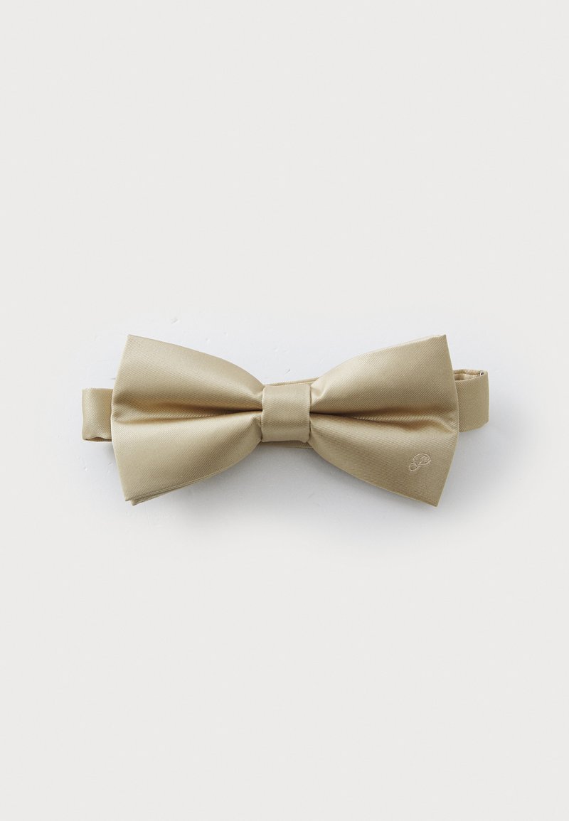 Noeud papillon en satin beige avec une texture lisse, doté d'un nœud central et d'une bande ajustable. Logo discret embossé sur le côté.