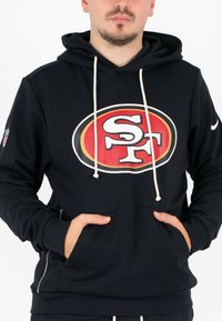 Zwarte hoodie van zacht materiaal, met een groot rood en wit NFL-logo op de voorkant, voorzien van witte trekkoorden en zijzakken.