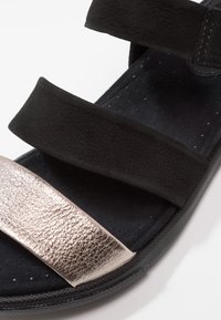 Mustat sandaalit, joissa on kolme säädettävää remmiä, ja joissa on teksturoitu metallinhohtoinen hopeakoriste. Pehmeä sisustus ja perforoitu muotoilu hengittävyyden lisäämiseksi.