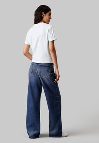 Lichtblauwe t-shirt met korte mouwen en een klassieke ronde hals, gecombineerd met brede donkerblauwe denim jeans. Casual, ontspannen pasvorm met zichtbare naden.