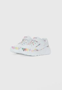 Sneakers bianchi Skechers con motivi a cuore multicolore lungo i lati, una striscia in velcro e dettagli in lacci su uno sfondo bianco.