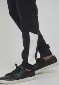 Marinblå joggebukser med hvit sidepanel, tapered fit, myk tekstur og ribbestrikkede mansjetter, kombinert med sorte lærsnickers.