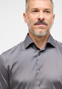 Grijze, langetermijns overhemd met een gladde textuur, knopenlijst vooraan en een klassieke kraag. Beschikt over een subtiele glans en zwarte knopen.