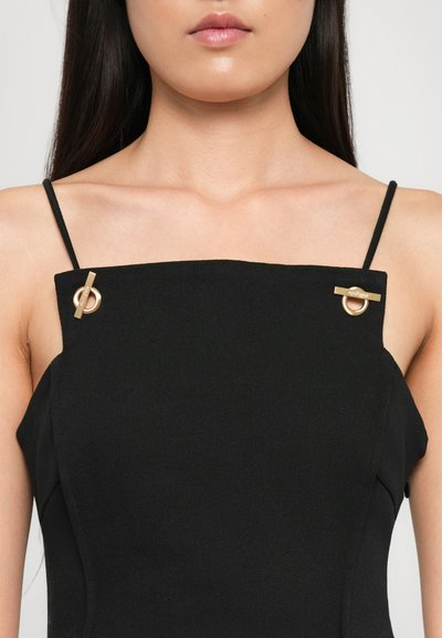 Robe noire avec un décolleté structuré droit, des fines bretelles et deux accents en hardware doré près des épaules. Tissu texturé.