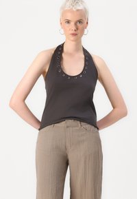 Dark gray sleeveless top with a rounded neckline and silver ring accents, paired with light beige, textured wide-leg trousers.