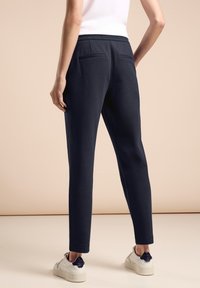 Marinträningsbyxor med en solid struktur, elastisk midja och två bakfickor, tillsammans med vita sneakers och en figurnära topp.