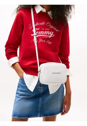 Kobieta w czerwonym dresie Tommy na białej koszuli, w dżinsowej spódnicy i białej torebce na ramię Tommy Jeans.