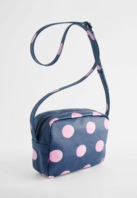 Zila crossbody soma ar rozā punktiņiem, taisnstūra forma, izgatavota no teksturēta materiāla, ar rāvējslēdzēju un regulējamu siksniņu.