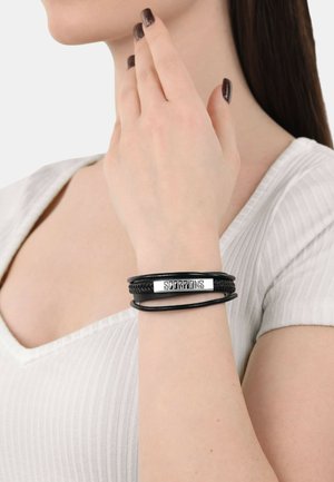 Black leather bracelet with a braided design and a silver-colored metal plate engraved with "SCORPIONS." Worn on a wrist.