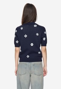 Tmavě modrý svetr s krátkými rukávy, s bílou květinovou výšivkou, žebrovaným límcem a lemem a zvlněnými okraji. Bavlněná směs.