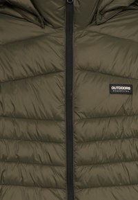 Veste matelassée vert olive avec une fermeture éclair noire et un écusson logo "OUTDOORS Expedition" sur la poitrine.