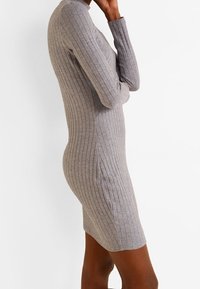 Robe à maille côtelée grise avec des manches longues, une silhouette ajustée et un col rond ; la texture met en valeur les rayures verticales et un tissu léger.