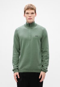 Olive green pullover sweater with a half-zip collar, ribbed cuffs, and a small black logo on the chest. Soft, textured fabric.