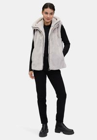 Kamizelka z sztucznego futra w miękkim szarym kolorze z kapturem, zamkiem błyskawicznym oraz dwoma bocznymi kieszeniami. Noszona na czarną bluzkę, w połączeniu z czarnymi spodniami i botkami.