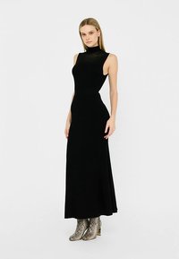 Robe noire sans manches à col montant et silhouette moulante, en tissu lisse. Associée à des bottes montantes imprimé serpent.