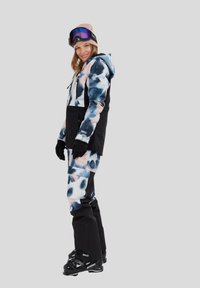 Skijas en broek in een kleurencombinatie van blauw, roze en zwart. Voorzien van een capuchon, zakken en handschoenen. Het materiaal lijkt duurzaam en waterbestendig.