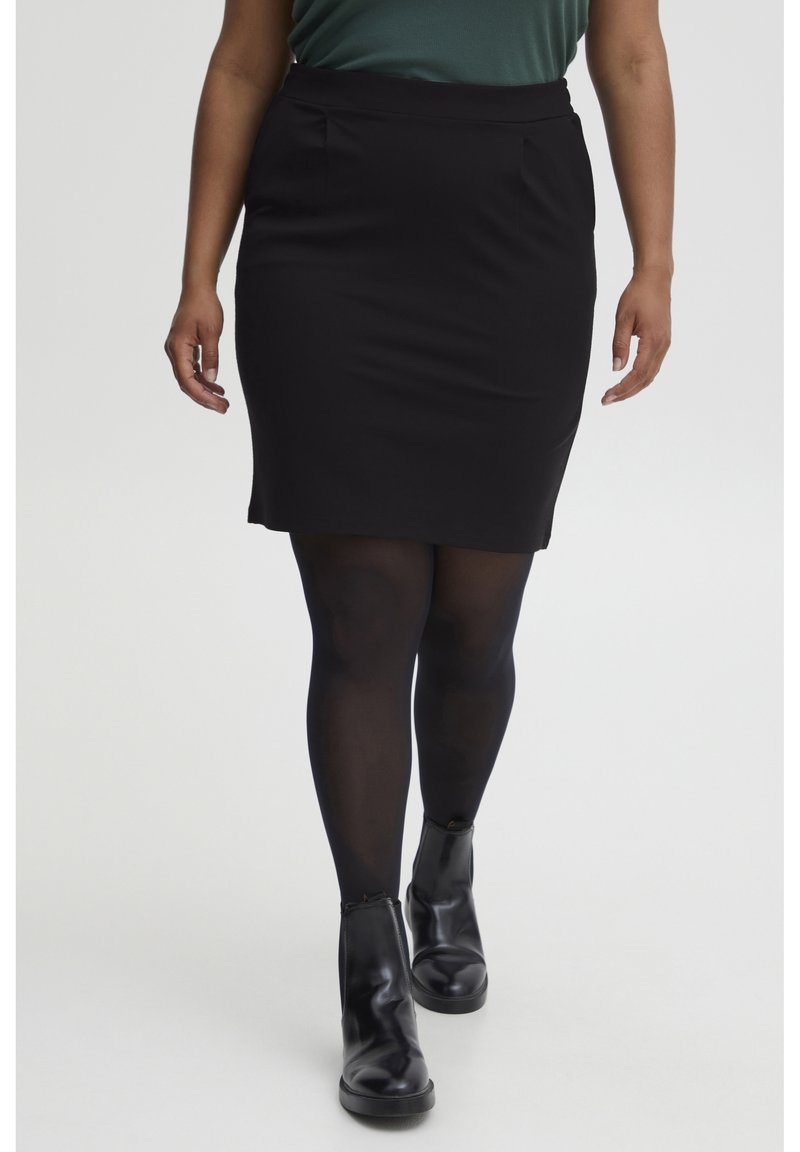 Zwarte aansluitende kokerrok met twee vo pockets, een gladde textuur en een lengte tot halverwege de dij. Gemaakt met zwarte panty’s en enkellaarsjes.
