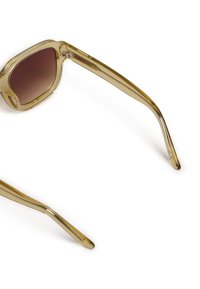 Gafas de sol con montura transparente y forma cuadrada, con lentes degradados en marrón y brazos alargados y elegantes. Textura suave en todo.