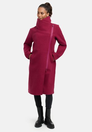 Maroon wool coat with a high collar, asymmetrical zip, and side pockets. Features a smooth texture and is paired with black ankle boots.