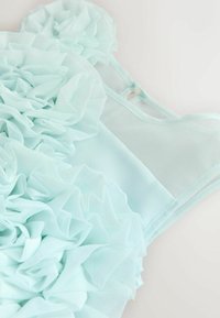 Hele roheline kleit, millel on tekstureeritud, kihilised volangid ühel küljel ja sile, läbipaistev osa teisel küljel. Reguleeritavad rihmad on lisatud.