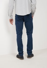 Marineblaue Baumwollhosen mit schmaler Passform und glatter Textur, ausgestattet mit Gesäßtaschen und kombiniert mit schwarzen Stiefeletten.