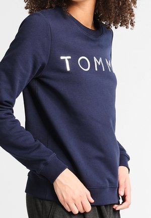 Felpa blu navy realizzata in morbido tessuto, con scollatura rotonda e polsini a coste. Davanti presenta la scritta bianca "TOMMY".