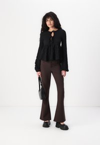 Black textured peplum top with long sleeves and a keyhole detail, paired with brown flared pants and chunky black platform shoes.