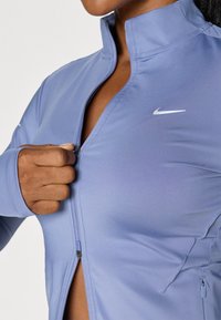 Light purple athletic jacket with a zip front, high collar, and subtle Nike logo. Features smooth fabric and tailored fit with side pockets.