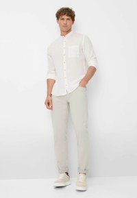 Witte linnen overhemd met staande kraag en een linkse borstzak, gecombineerd met lichtbeige chinos en crèmekleurige sneakers.
