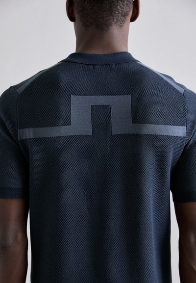 Polo de manga corta azul marino con un patrón de punto texturizado, que presenta un diseño geométrico gris en la parte posterior y puños acanalados sólidos.