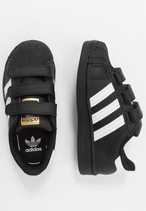 Czarne dziecięce tenisówki Adidas z białymi paskami, paskami na rzep i złotym logo Adidas, pokazane z góry i z boku.