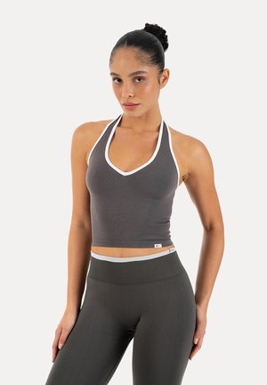 Femme portant un crop top gris à col halter avec un liseré blanc et un legging taille haute assorti sur fond blanc uni.