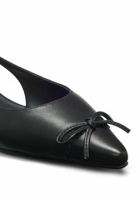 Chaussure plate en cuir noir à bout pointu avec un petit nœud sur le devant et une bride arrière.