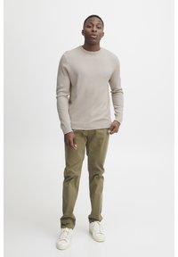 Beige, strukturerad stickad tröja med rund halsringning, ihop med olivgröna rakbenade byxor och vita sneakers. Enkelt och avslappnat design.