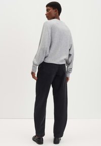 Felpa grigia con maniche lunghe e arricciate, abbinata a jeans scuri. L'outfit presenta una vestibilità rilassata e dettagli di cucitura sottili.