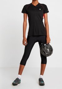 Svart cykeltröja med röda detaljer, kortärmad, och delvis dragkedja. Bärs med svarta cykelbyxor och hjälm, med texturerade skor.