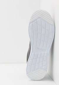 Sål af en grå sneakersko med hvidt slidbane, der har diagonale og diamantformede mønstre samt mærkenavnet "Kappa" indgraveret i midten.