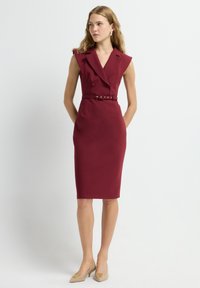Robe sans manches bordeaux avec un col à revers, des boutons doublés et une ceinture à la taille ; texture lisse et design midi.
