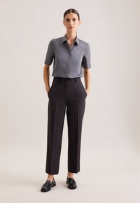 Camicia grigia a maniche corte con bottoni e pantaloni neri su misura, con taglio dritto e texture liscia, abbinati a mocassini neri.