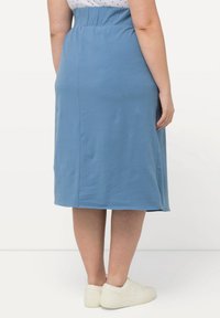 Gonna midi blu in jersey con vita elasticizzata, caratterizzata da una texture liscia e spacchi laterali per facilitare i movimenti. Indossata con sneaker bianche.