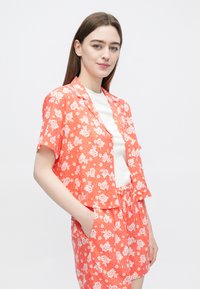 Röd blommig kortärmad skjorta med vita blommor och en avslappnad passform, kombinerad med matchande shorts med elastisk midja och fickor.