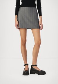 Grijze mini-jurk met een fijne streep en een getailleerd silhouet, gecombineerd met chunky zwarte plateau-schoenen met enkelbandjes en een glanzende afwerking.