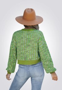 Groene gebreide trui met een gestructureerd ruitpatroon, ronde halslijn en verlaagde mouwen. Gecombineerd met lichtblauwe aansluitende jeans.