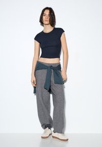 Námořnické zkrácené tričko, šedé volné tepláky a modrozelená kostkovaná košile zavázaná v pase. Outfit doplňují bílé tenisky.