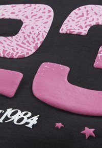 T-shirt in tessuto nero con grandi lettere e numeri testurizzati rosa, "1984," e piccole stelle rosa, evidenziando un design grafico audace.