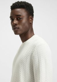 Strickpullover in Weiß mit strukturiertem Fischgrätenmuster, rundem Ausschnitt und taillierter Silhouette.