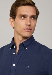 Camicia azzurra navy in cotone con finitura testurizzata. Presenta un colletto a punta, bottoni bianchi e un piccolo logo sul petto.
