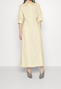 Gul bomullsklänning med krage, knäppning fram och bälte i midjan. Matchas med svarta och vita zebra-mönstrade klackskor med spetsig tå.