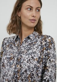 Cămașă cu butoni florală, albă, cu modele negre, albastre și galbene; material moale, cu guler și mâneci ușor bufante.