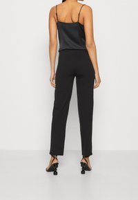 Haut caraco en satin noir à fines bretelles, associé à un pantalon noir sur mesure. Les accents remarquables incluent des chaussures à talons uniques.